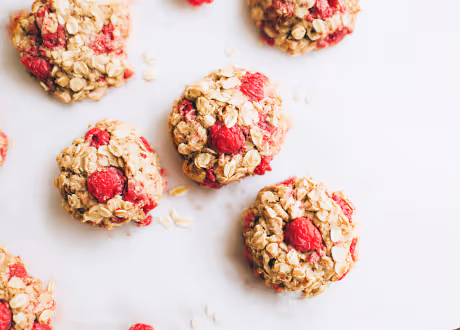Oatmeal cookies with fresh raspberries on a white surface.