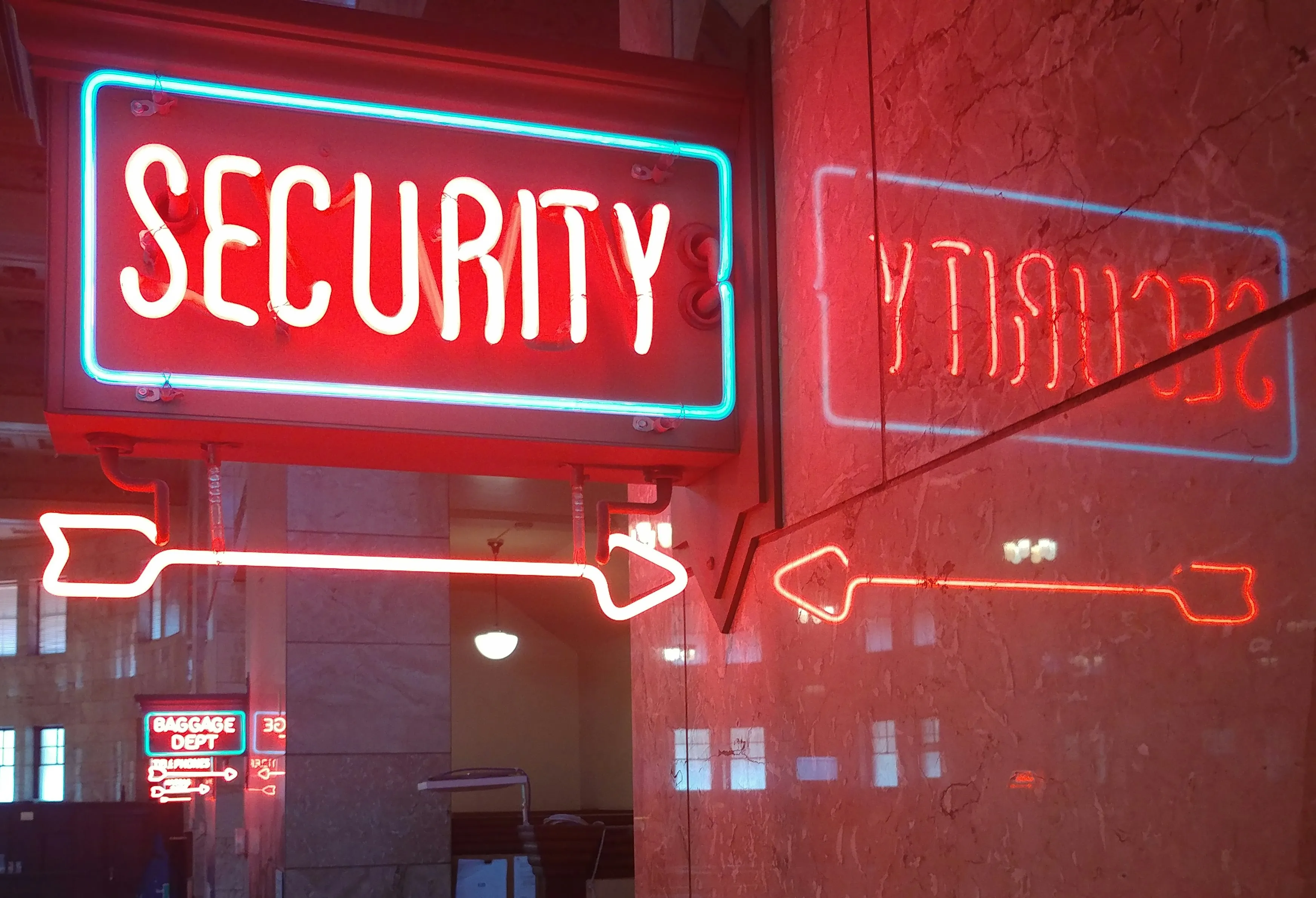 Neon sign reading SECURITY with a horizontal arrow, reflected on a marble wall.
