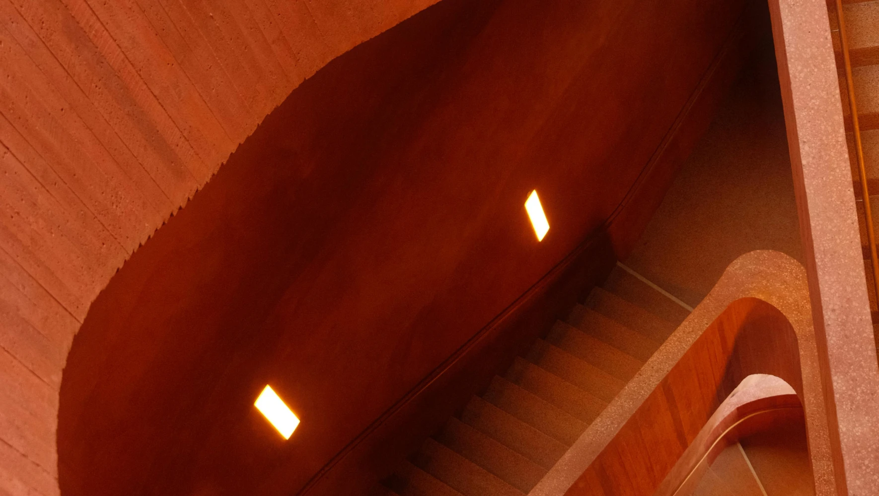Curved interior concrete staircase with warm orange lighting and textured walls.