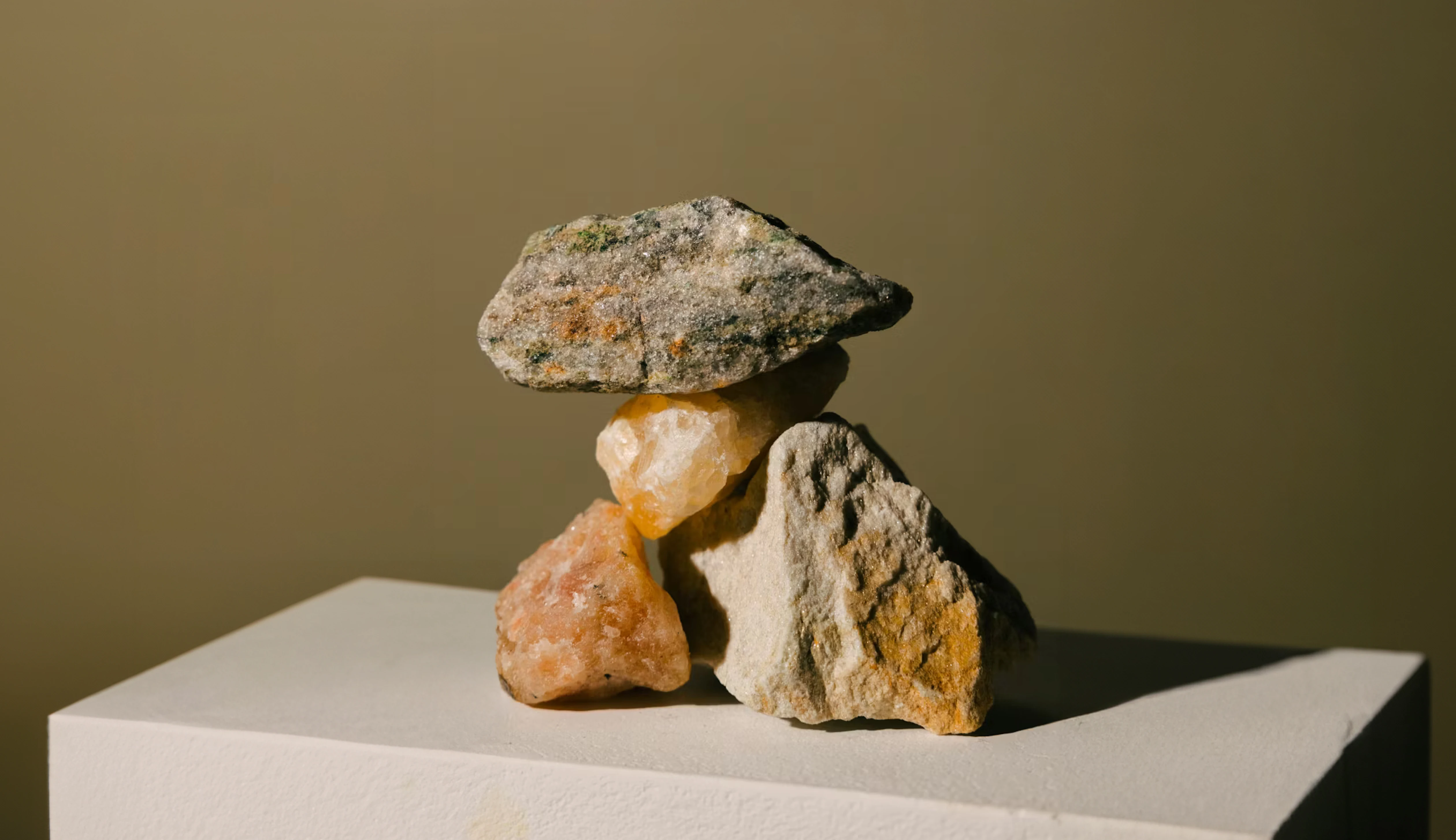 Stack of stones balanced on a white pedestal against a brown background.