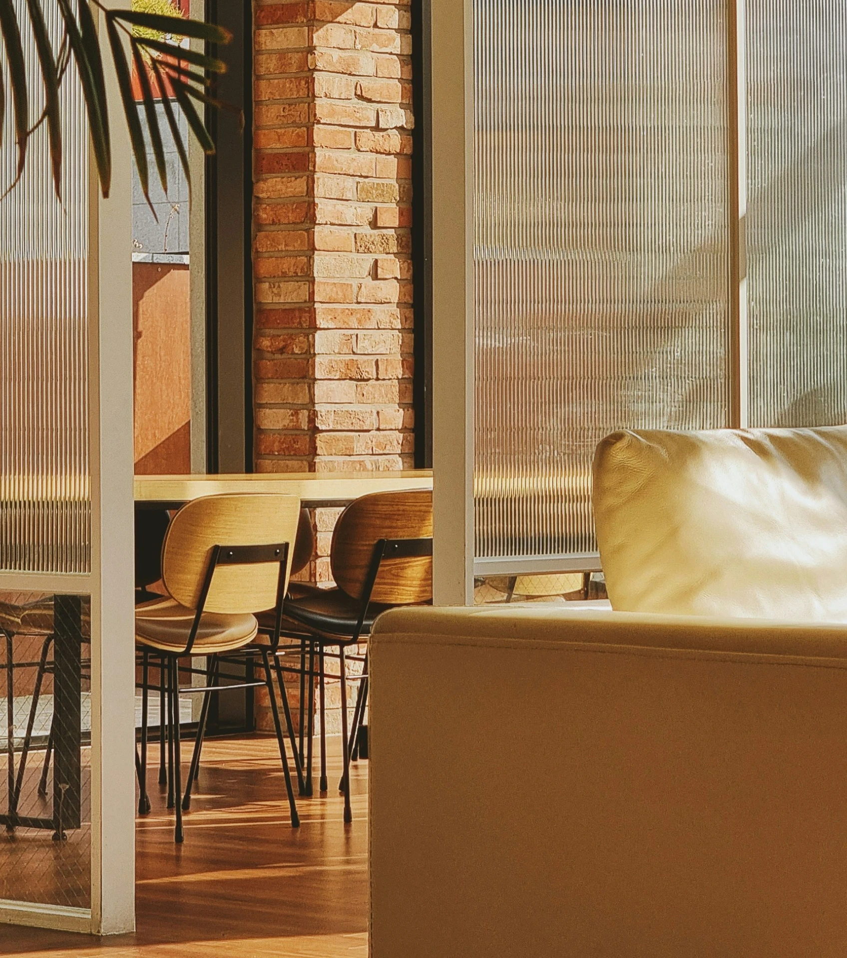 Sunlit dining area with wooden chairs, a table, brick wall, and a beige sofa in foreground.