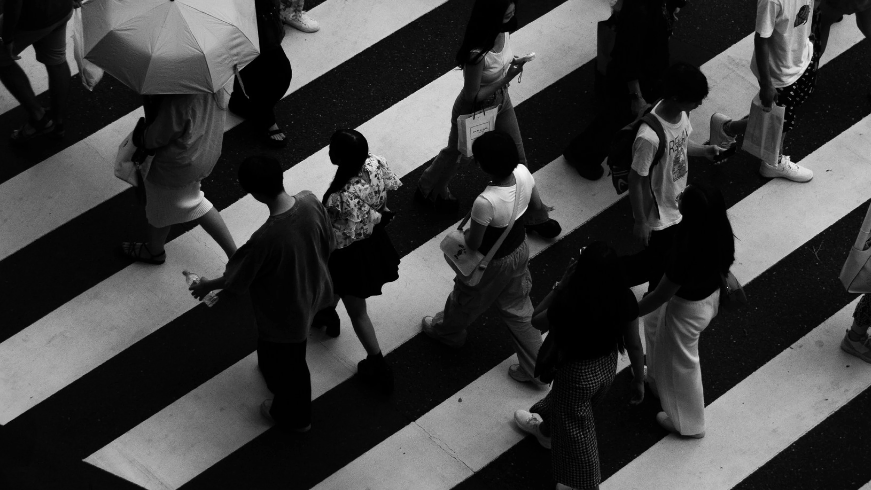 Black and white photo of people walking across a zebra crosswalk from above.