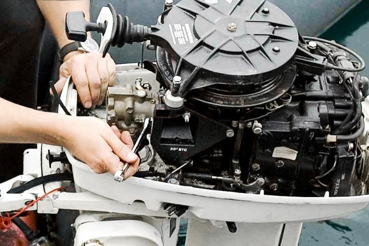 Close-up of a technician's hands using a wrench on the powerhead of an outboard motor with the cowling removed.