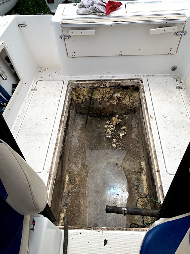 Open deck hatch on a center-console boat revealing the empty, corroded fuel tank compartment during a fuel system service