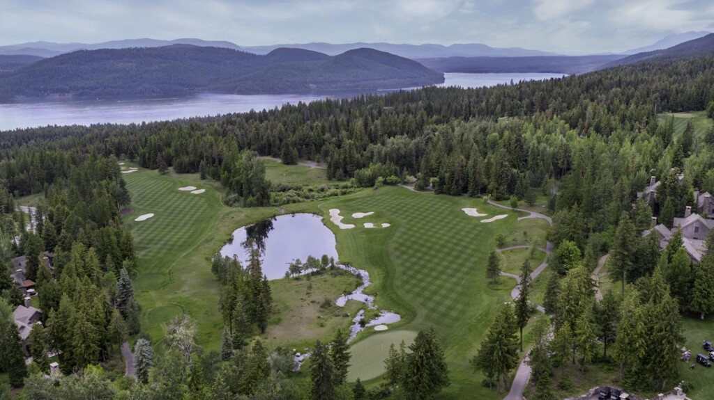 Aerial view of Iron Horse golf course in Whitefish, Montana, surrounded by forest, with a pond and mountains in the background.