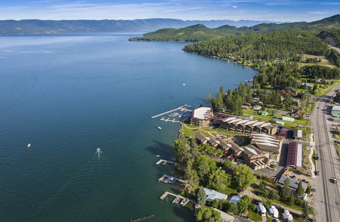 Aerial view of Lakeside, Montana, with docks, boats, forest, buildings, and a road alongside the water.