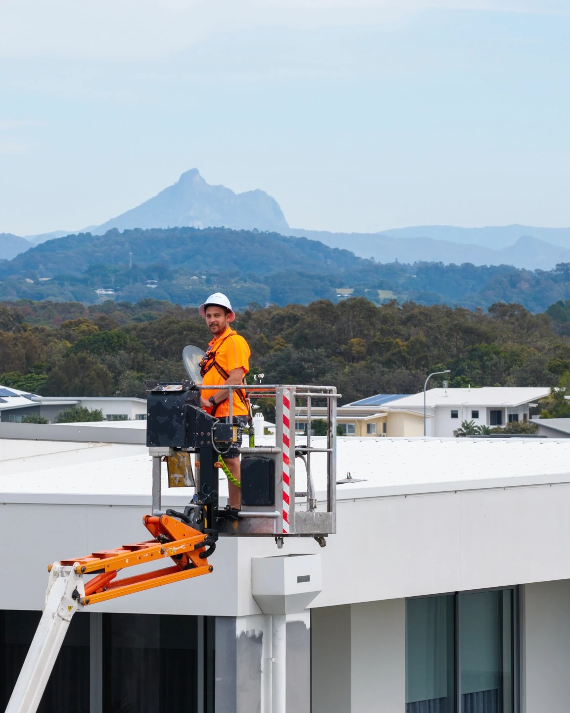 Painter on elevated work platform painting rooftop of apartment building with mountain view