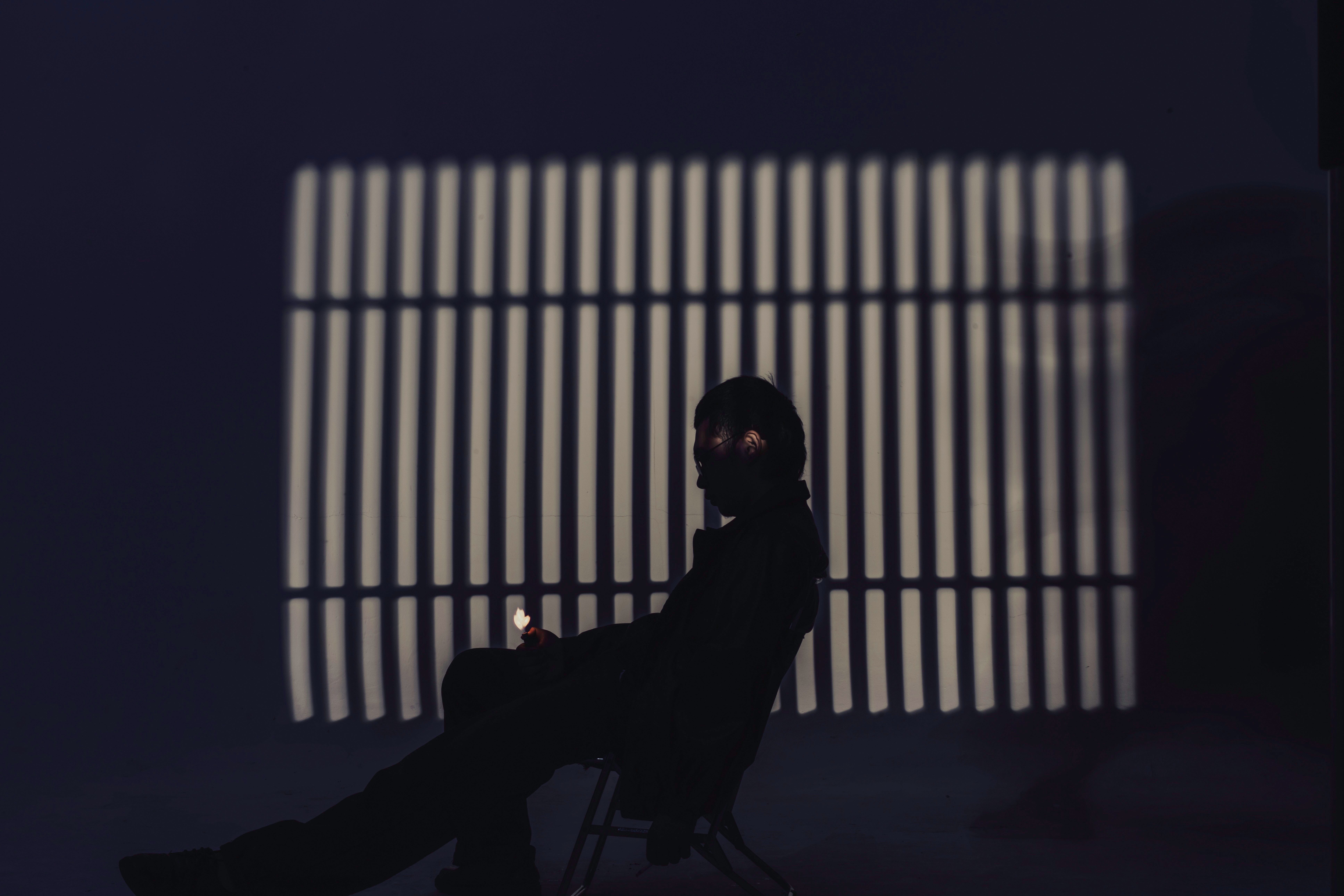 A silhouette of an adult seated indoors, casting shadow bars on the wall