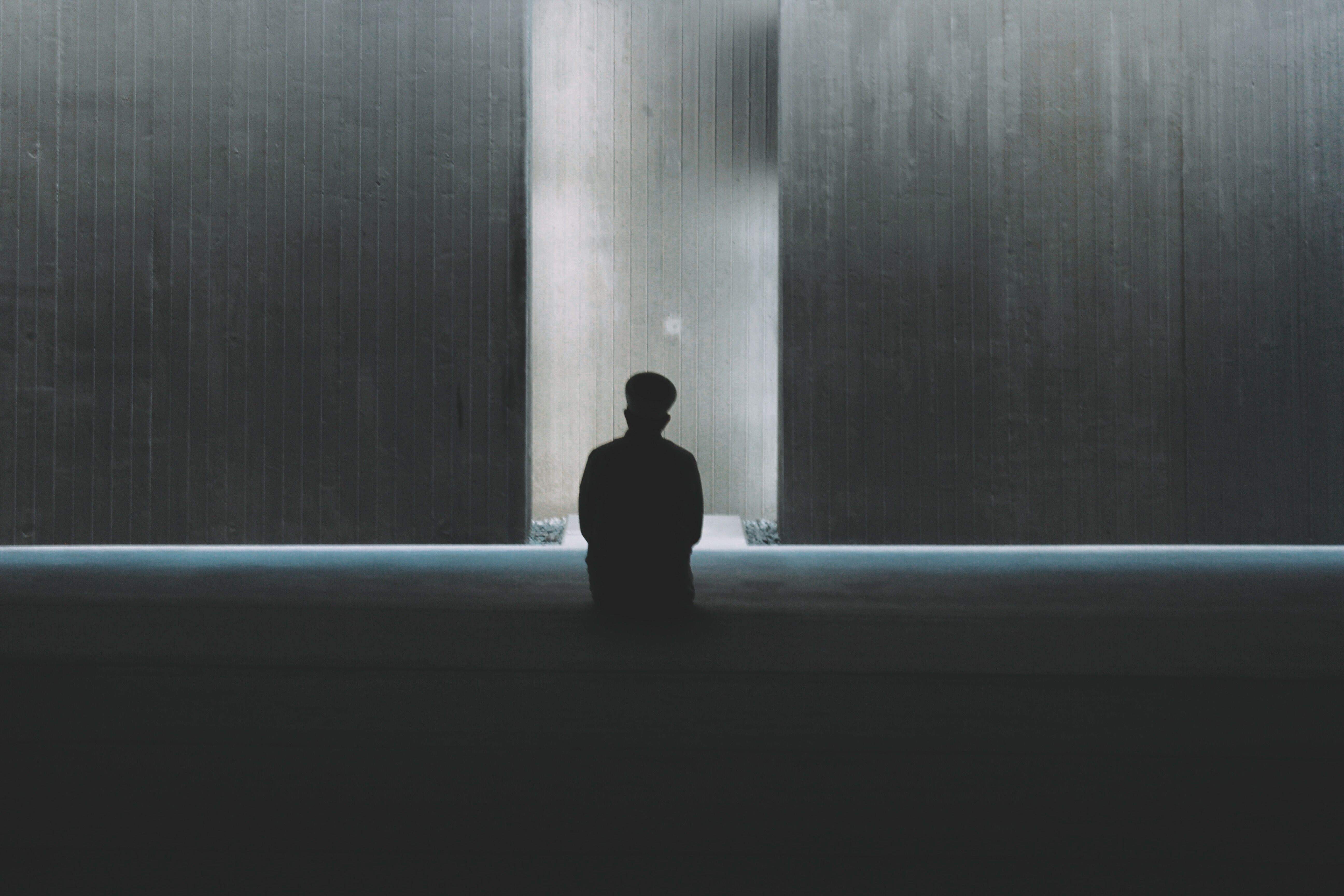 Silhouetted person sitting in a dark minimalist space with light reflection on walls.