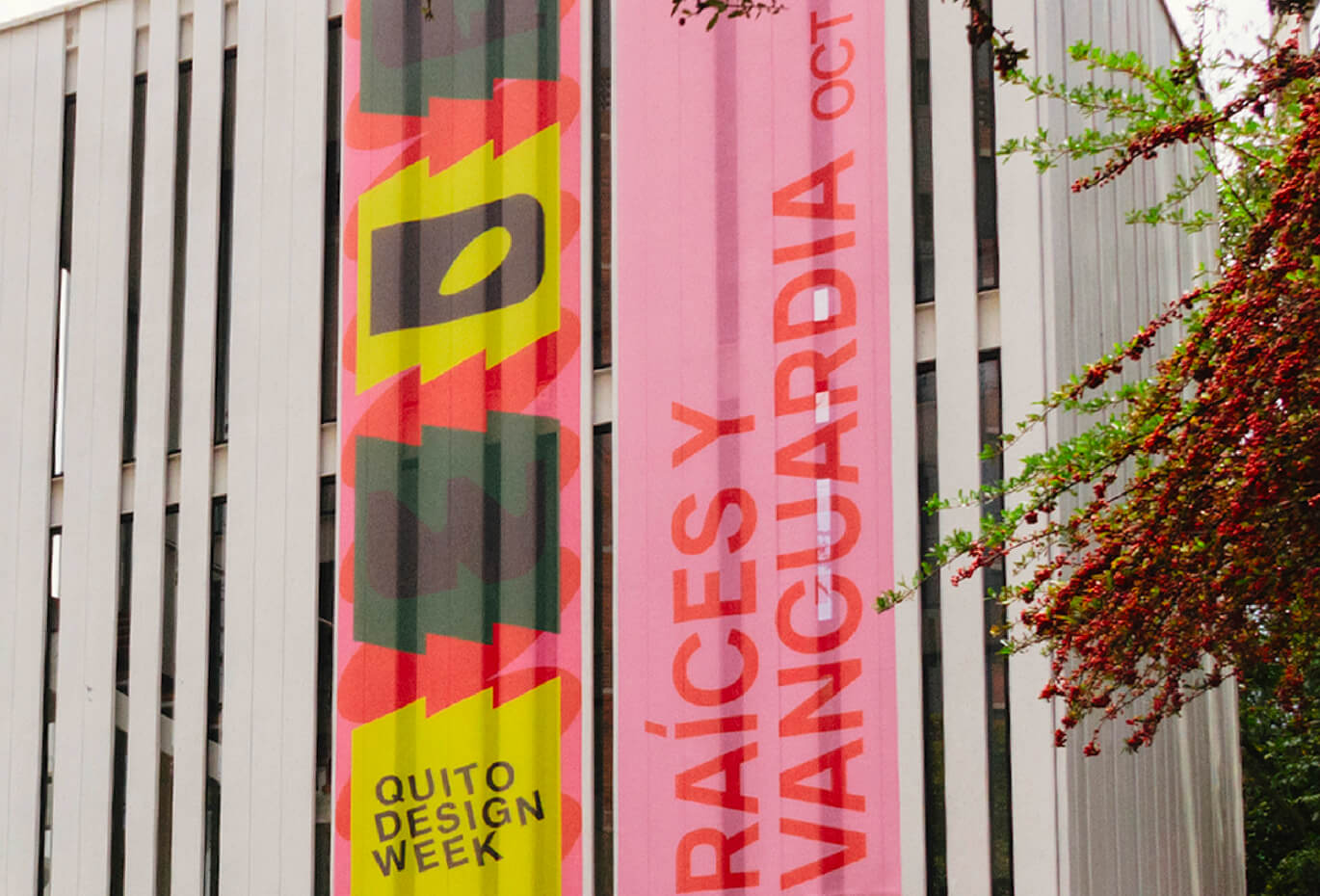 Vertical pink and yellow Quito Design Week banners displayed on a building facade, featuring bold experimental typography and graphic shapes.