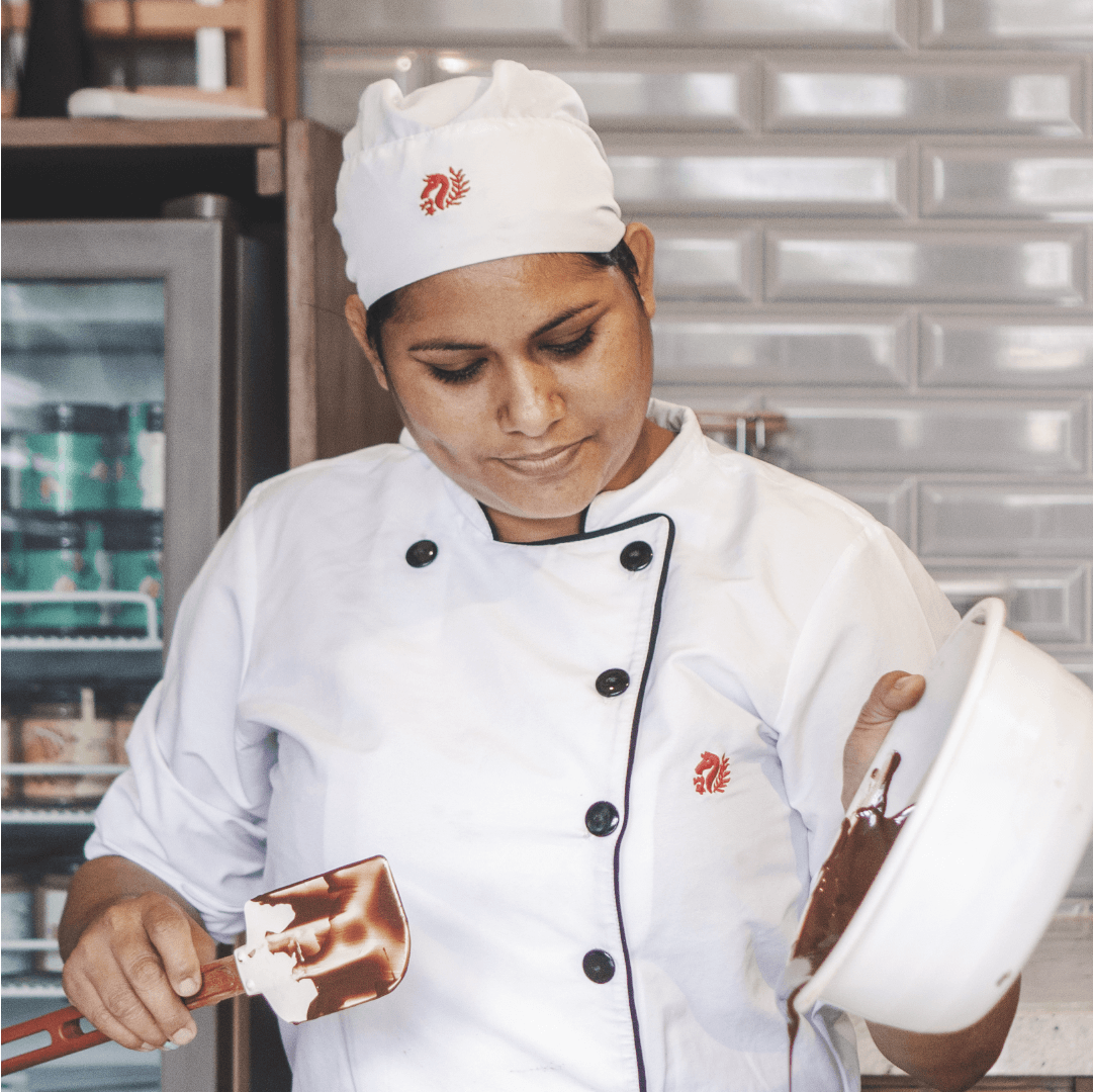 Chef uniform branding for La Danesa by Lunalunares, showing embroidered brand marks on a white culinary uniform worn by a chef preparing chocolate in a kitchen.