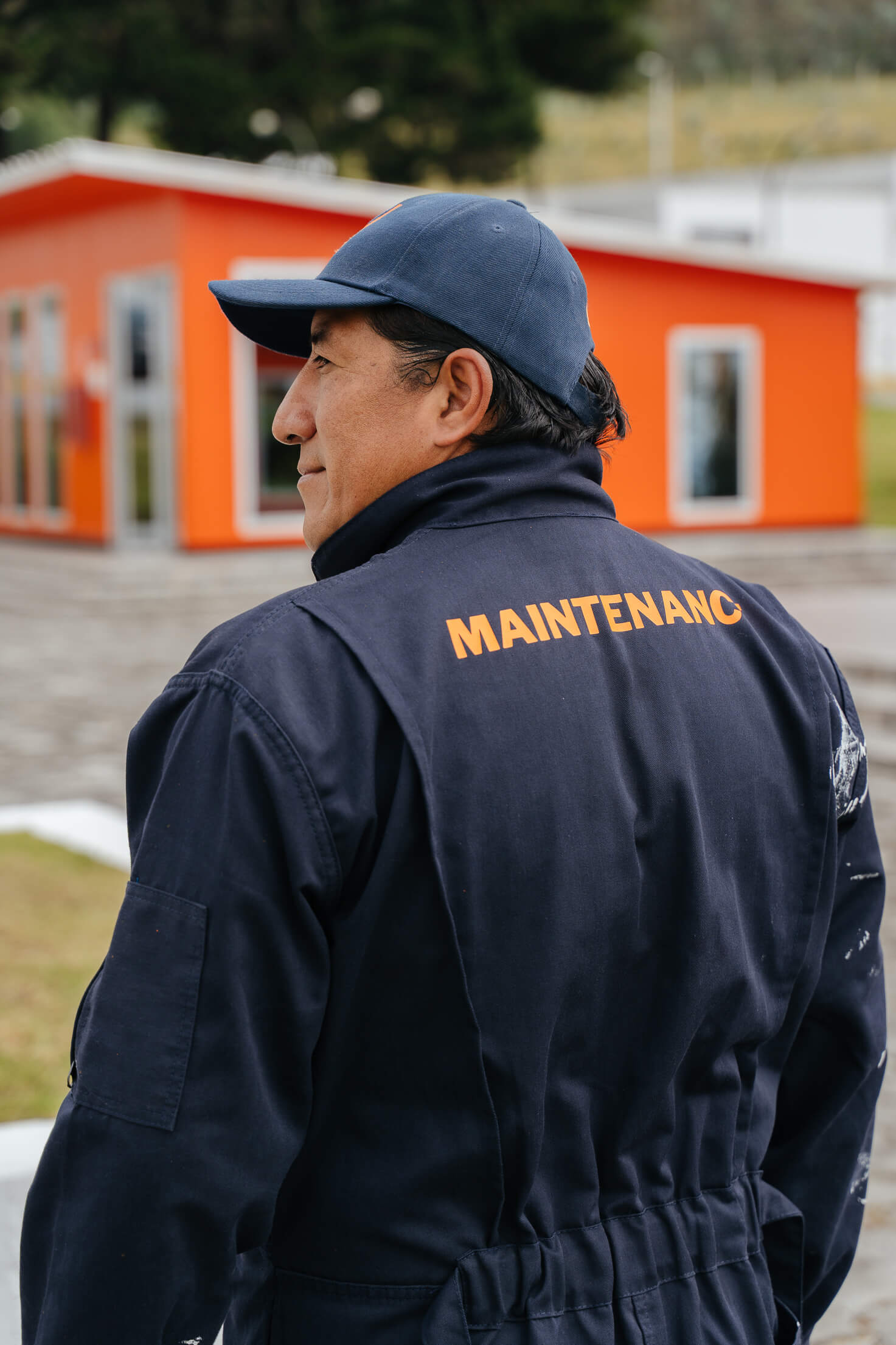 Maintenance uniform brand application for Universidad de los Hemisferios by Lunalunares, showing a staff member wearing a navy uniform with orange typography on campus.