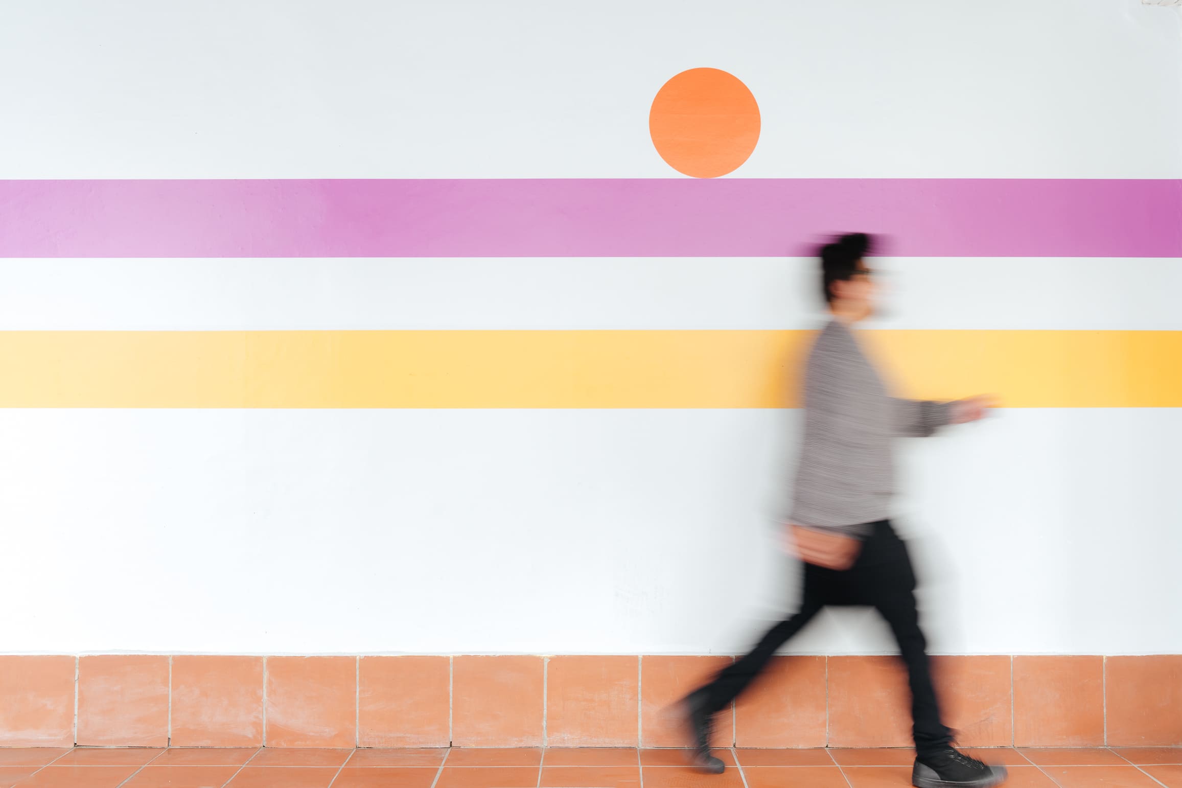 Campus color system for Universidad de los Hemisferios by Lunalunares, showing a person walking past a striped wall with orange, pink, and yellow institutional accents.