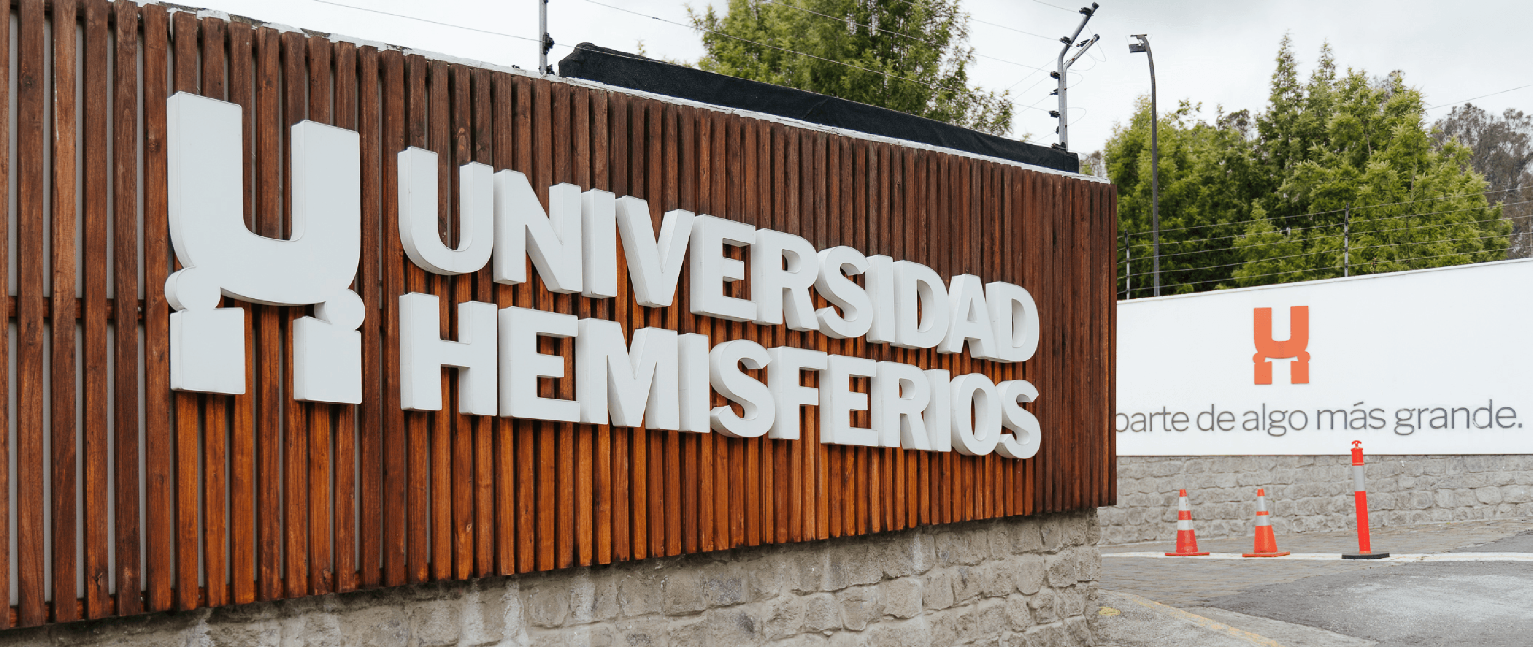 Main campus entrance signage for Universidad de los Hemisferios by Lunalunares, showing large dimensional letters on a wooden facade and the institutional tagline in the background.