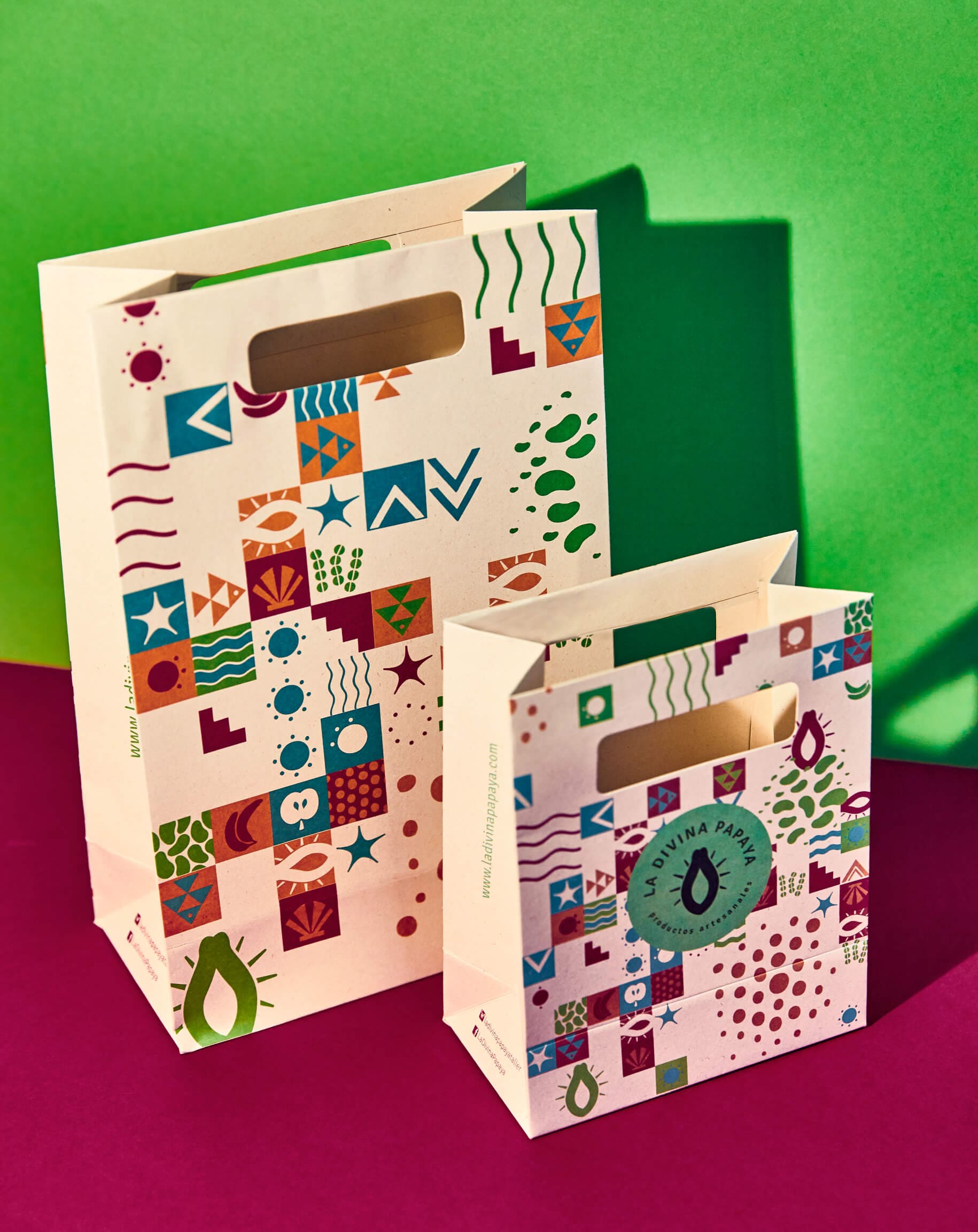 Branded paper bags for La Divina Papaya by Lunalunares, featuring colorful packaging design with geometric patterns, artisan-inspired symbols, and bold product branding on a vibrant green and magenta studio background.