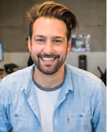 Smiling man with beard and mustache wearing a light blue shirt and white t-shirt.