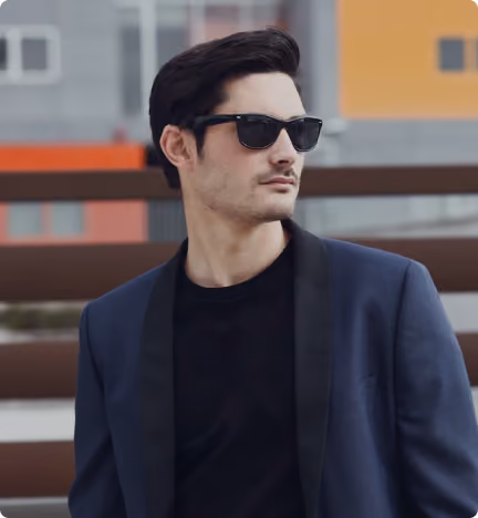 Man wearing sunglasses and a navy blazer looking sideways against an urban background.
