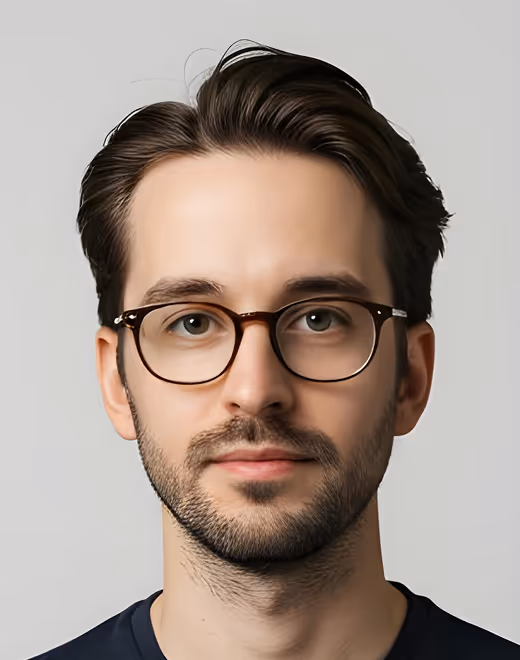 Young man with dark hair and beard wearing round glasses and a dark shirt, facing front.