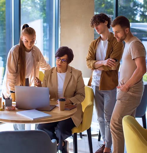 Four people gathered around a laptop in a bright room, collaborating and discussing work.