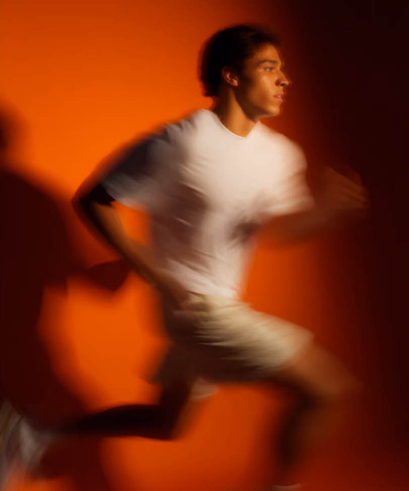 Blurred image of a young man running against an orange background.