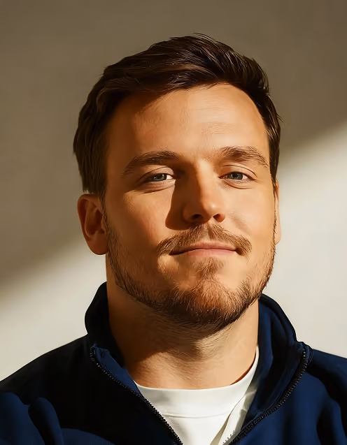 Close-up of a man with light beard and mustache, wearing a navy jacket and white shirt.