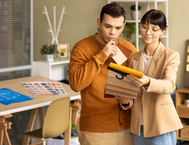 Man and woman examining color swatches in a design office with a table and chair in background.