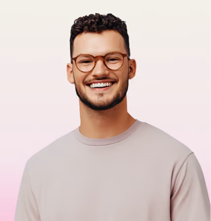 Smiling man with curly hair, beard, and glasses wearing a light gray shirt against a light background.