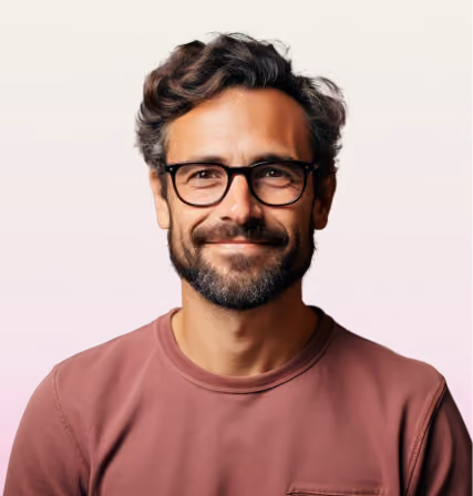 Smiling man with glasses, dark wavy hair, and beard wearing a mauve crew-neck shirt.