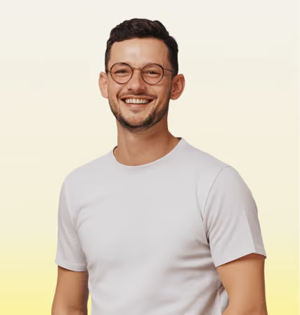 Smiling man with short dark hair and glasses wearing a plain light gray t-shirt against a light background.