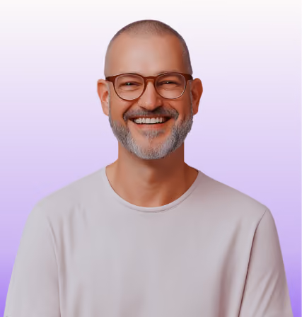 Smiling bald man with gray beard and glasses wearing a white shirt against a purple gradient background.