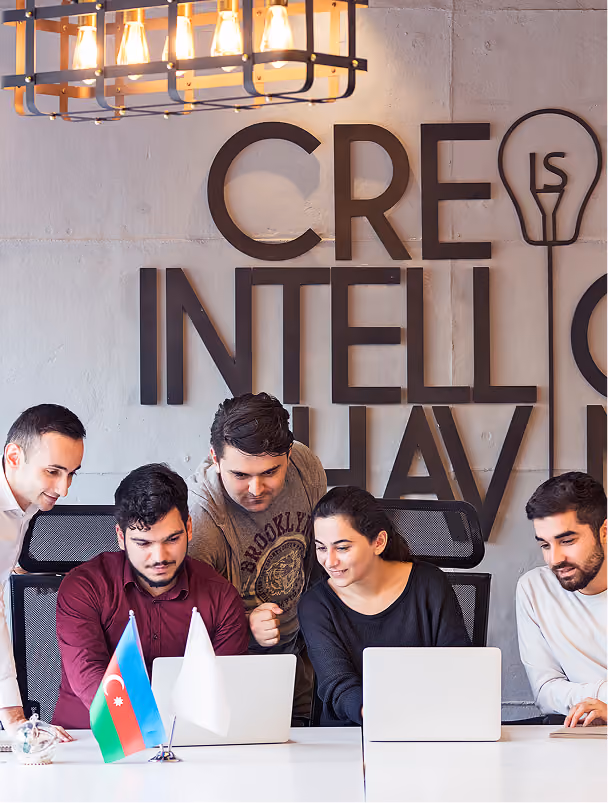 Group of five young people working together on laptops at a table with Azerbaijani flag.