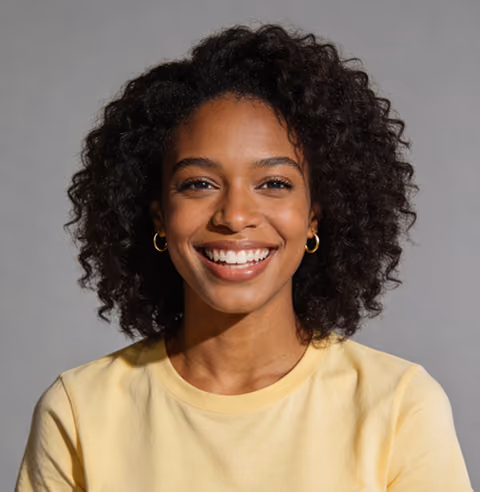 Smiling woman with curly hair wearing a yellow shirt and gold hoop earrings against gray background.
