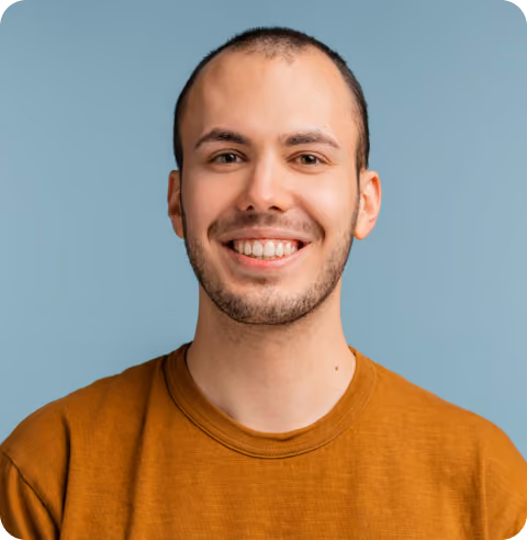 Smiling young man with short hair, beard, and brown shirt against a blue background.