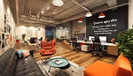 Modern office lounge with orange chairs, wooden tables, large chalkboard wall, and hanging lights.