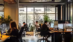 Office space with workers at desks and large windows revealing trees outside.
