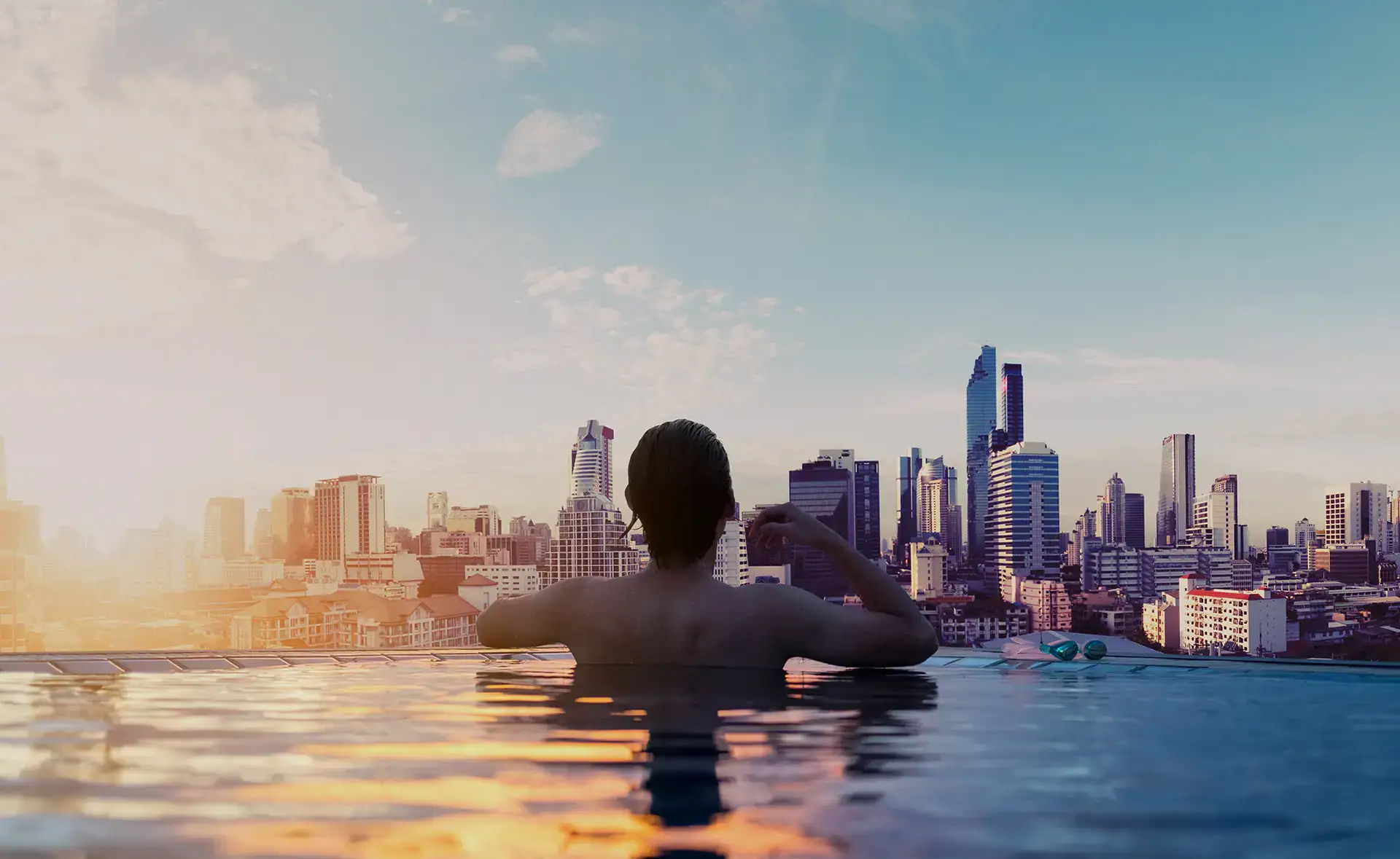 Traveler relaxing in an infinity pool overlooking a city skyline at sunset