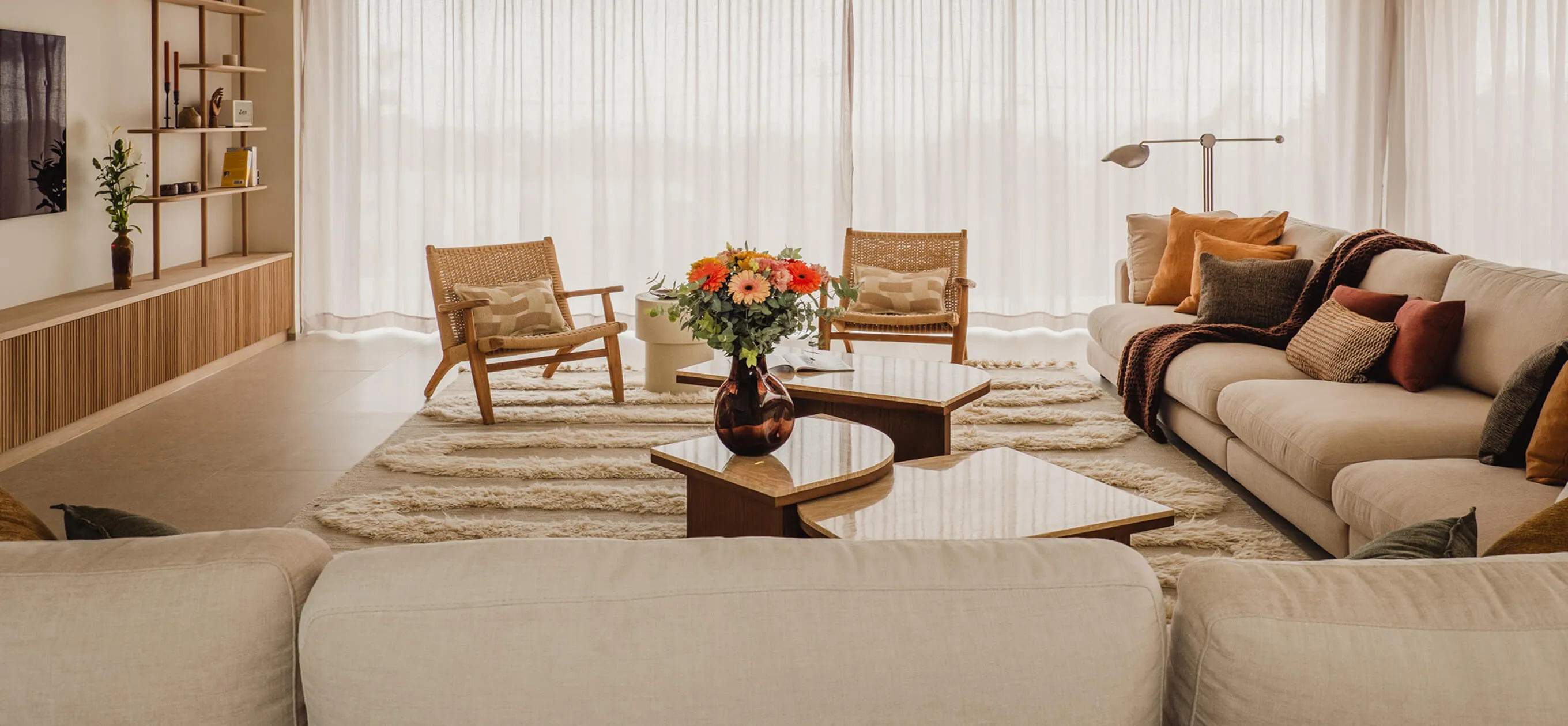 Full panoramic view of a luxury living room interior design in Ibiza at Villa Benimussa, showcasing bespoke organic wooden coffee tables, a plush sectional sofa, and textured Balearic rugs.