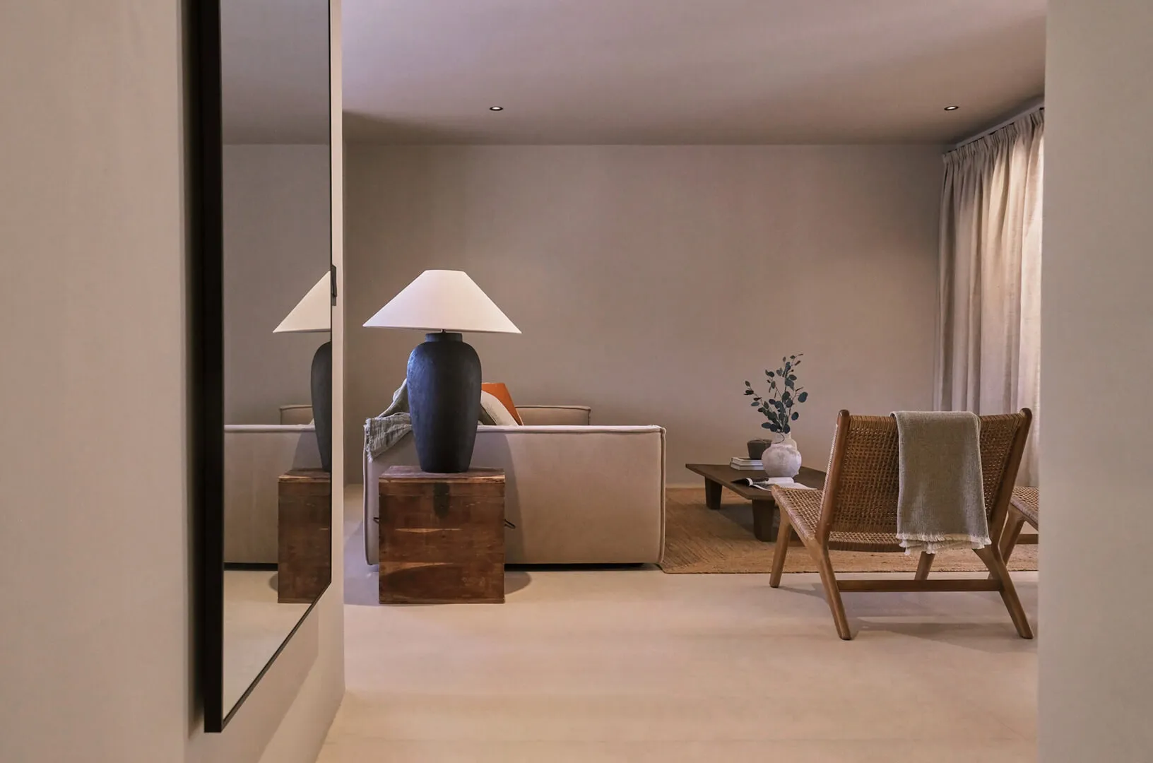 Cozy luxury living room design at Sa Caleta, Ibiza, featuring a neutral sofa, a large black ceramic table lamp, and an antique wooden chest.