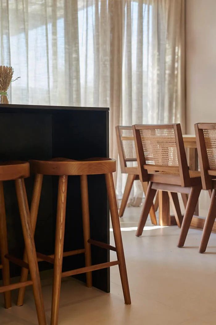 Close-up of custom wooden bar stools at a modern black kitchen island within the Sa Caleta villa project in Ibiza.