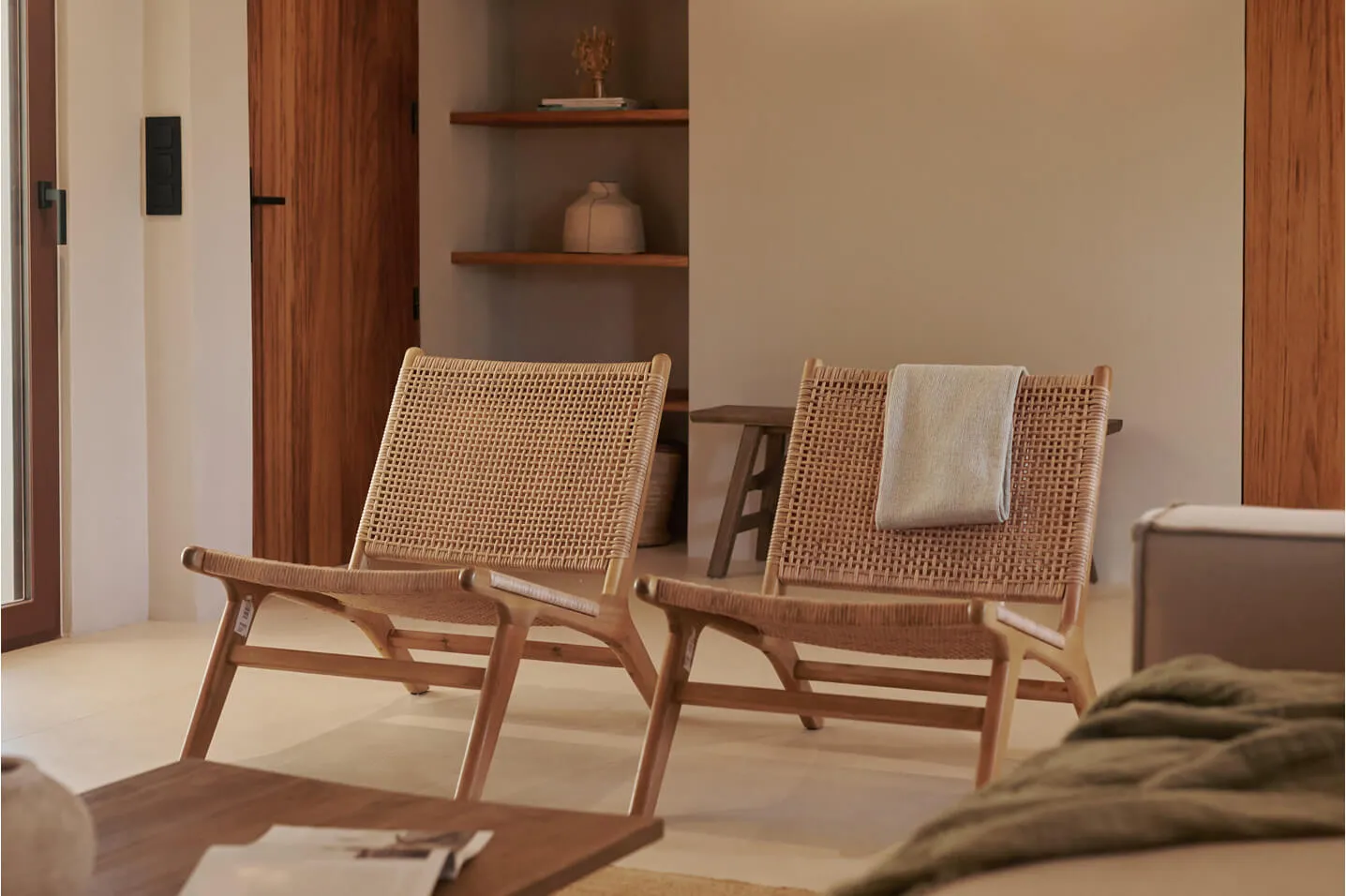 Minimalist interior architecture and styling at Sa Caleta, Ibiza, showcasing twin woven lounge chairs and custom warm wood doors.