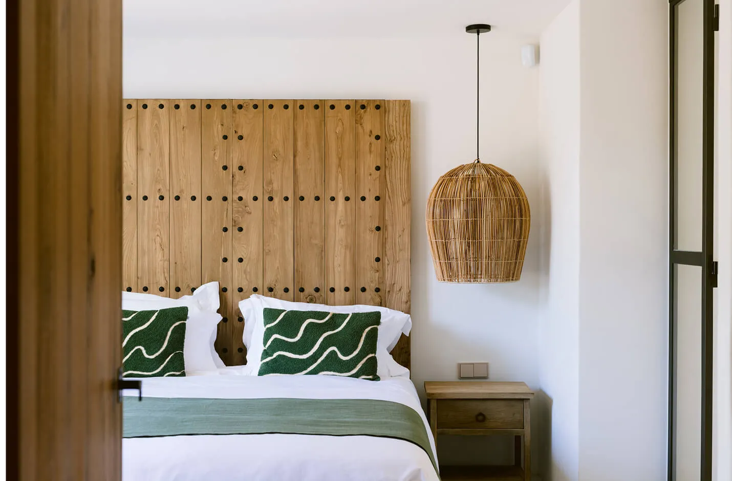 Luxury villa bedroom interior design at Villa Benimussa, Ibiza, showcasing a bespoke rustic wood headboard with studs and a woven rattan pendant light.