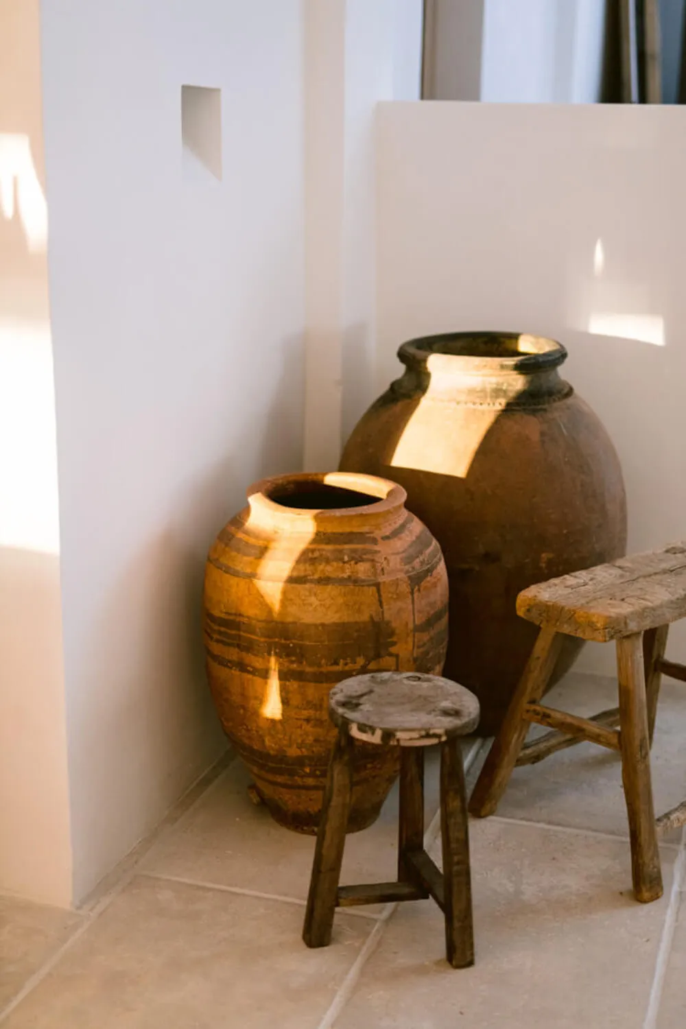 Luxury interior design details at Villa Benimussa in Ibiza, showing rustic antique terracotta urns and old wooden stools in natural sunlight.