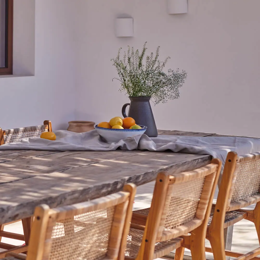 Rustic Mediterranean dining area at the Sa Caleta country home in Ibiza by Studio Moravová, featuring a reclaimed wooden table, woven chairs, and natural styling.