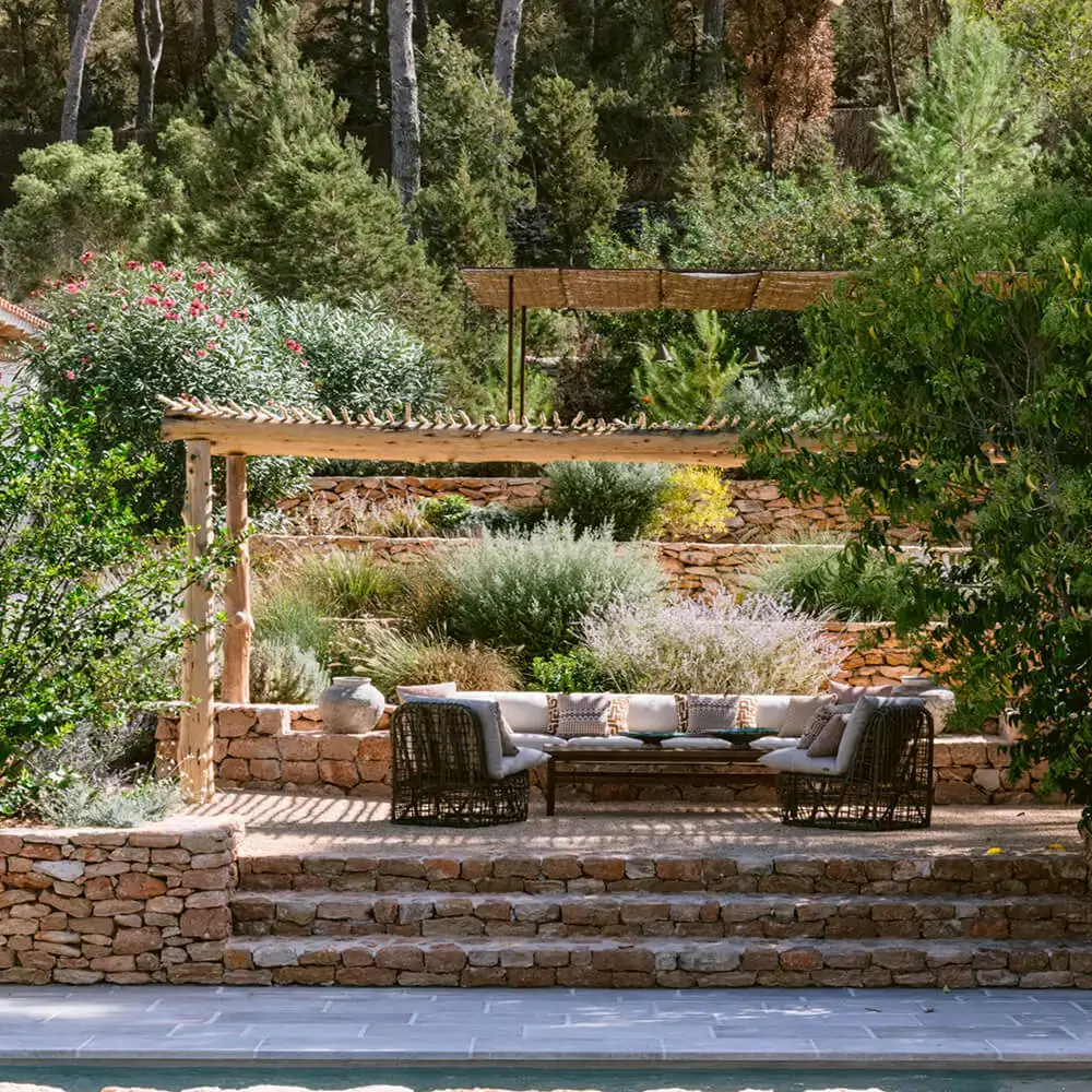 Luxury outdoor lounge and patio design at the Villa Benimussa residential project in Ibiza by Studio Moravová, featuring traditional stone walls and lush Mediterranean landscaping.