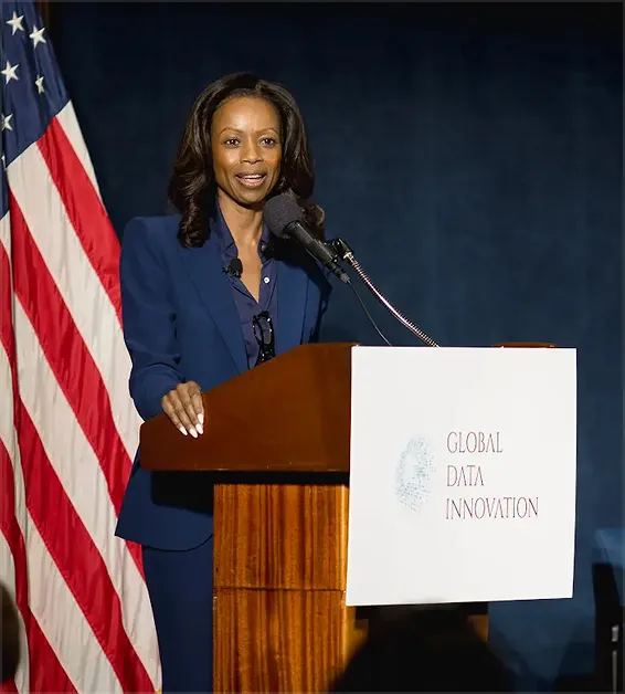 Woman in blue suit speaking at a podium with a Global Data Innovation banner and U.S. flag behind her.