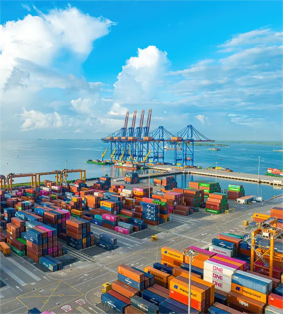 Cargo shipping port with colorful stacked containers and large blue cranes by the water under a blue sky.