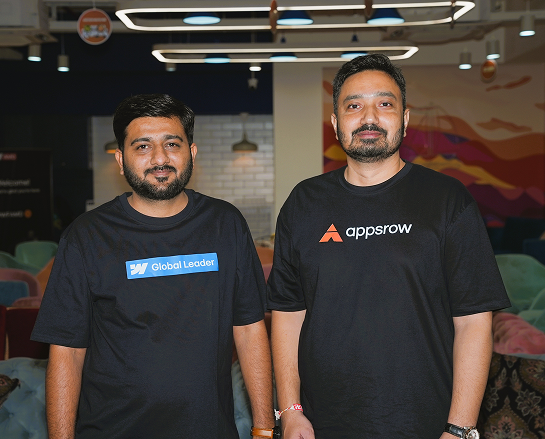 Two men posing indoors wearing black t-shirts with logos 'Global Leader' and 'appsrow'.