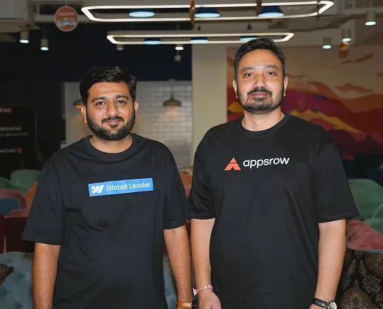 Two men posing indoors wearing black t-shirts with logos 'Global Leader' and 'appsrow'.