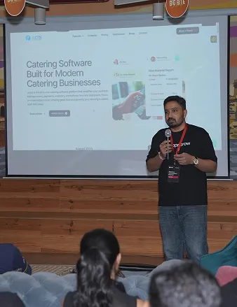 Man giving a presentation with catering software displayed on a large screen behind him.