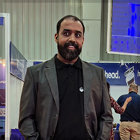 Man with beard wearing a gray blazer and black shirt standing indoors at a public event.